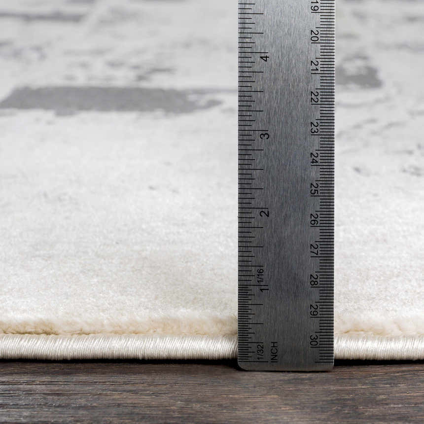 Close-up of Lares Area Rug pile height in light beige and gray with a ruler showing the thickness. Pile