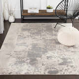 Living room scene with a charcoal and beige Lares Area Rug, black chair, and knit pouf. Roomscene-Rectangle