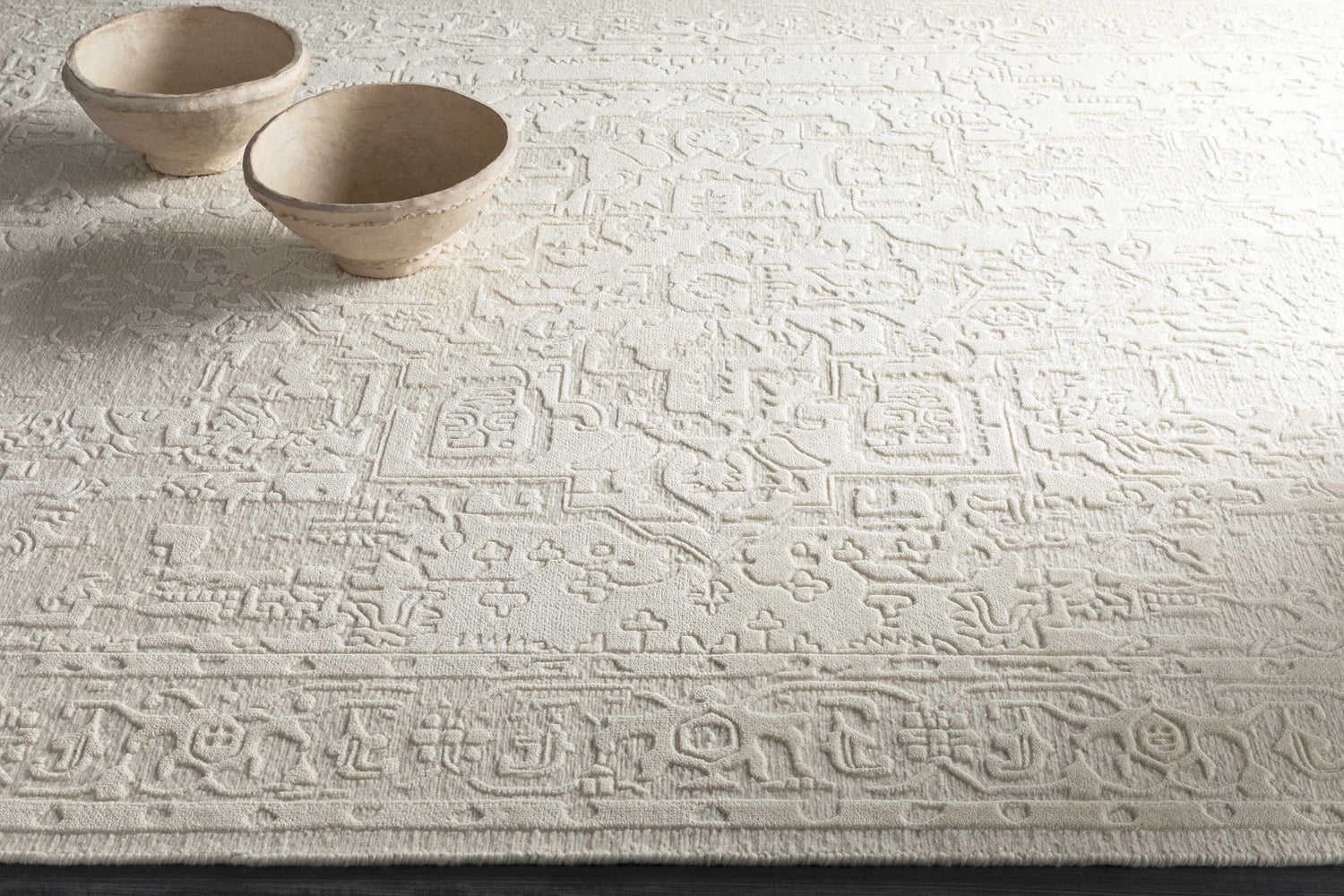 Close-up of the ivory Larimer Area Rug with a raised, textured pattern and two decorative bowls. Styleshot