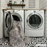 Farmhouse laundry room with Athor Washable Rug being put in the washing machine. Black and white patterned tile floor. Washing-Machine