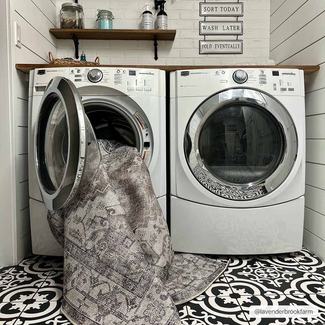 Farmhouse laundry room with Athor Washable Rug being put in the washing machine. Black and white patterned tile floor. Washing-Machine