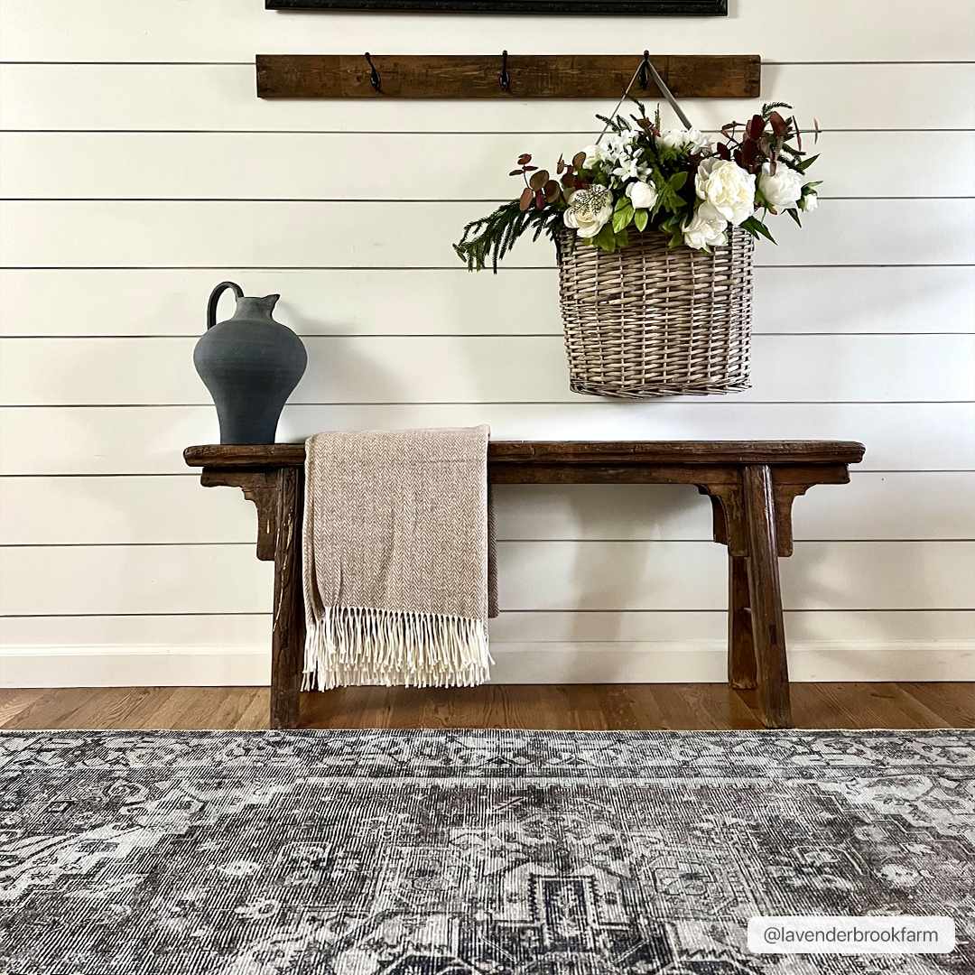 Entryway with a dark gray Athor Washable Rug, wood bench, throw blanket, and floral basket. Farmhouse style. Roomscene-Rectangle