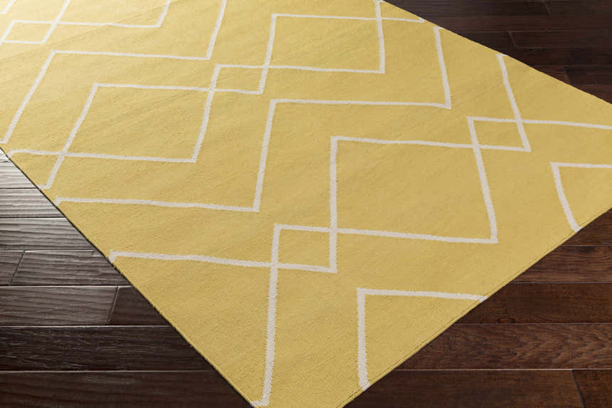 Close-up of the hand-woven Leatherwood Area Carpet. Off white geometric pattern on a tan, 100% cotton rug. Contemporary style. Corner
