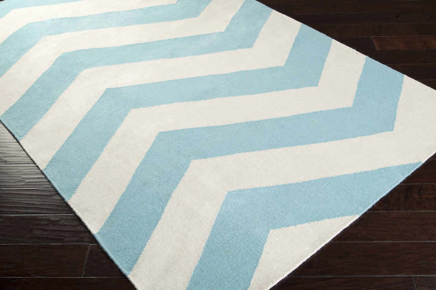 Close-up of the Lerona Area Rug. Hand-woven wool rug with aqua and white chevron pattern on a dark wood floor. Corner