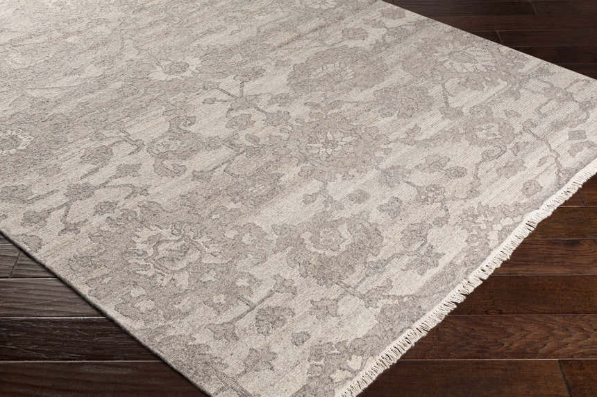 Close-up of the beige and charcoal Lerwick Carpet, a hand-knotted wool rug with a traditional floral pattern and fringe. Corner