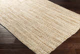 Close-up of a hand woven Leyton Natural Jute Rug showing ivory and tan tones, and natural texture on dark wood floor. Corner