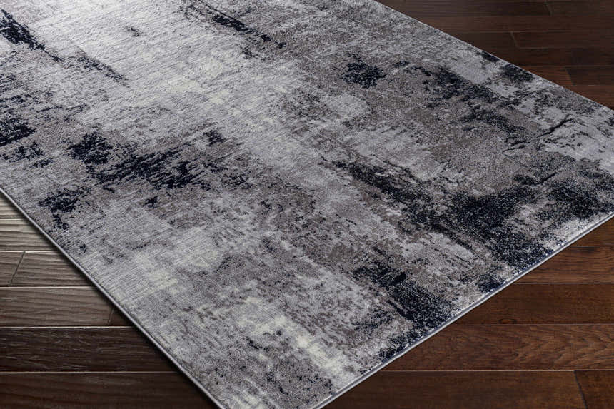 Close-up of Limao Abstract Denim Area Rug on dark wood floor. Contemporary style rug with gray, cream, and denim colors. Corner