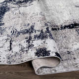 Close-up of the Limao Abstract Denim Area Rug showing its denim, cream, and gray abstract pattern and soft texture. Fold