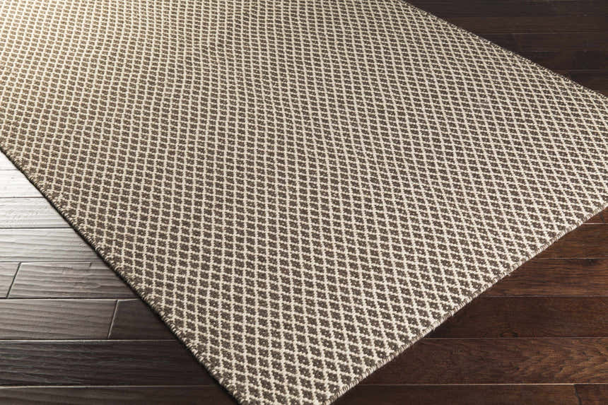 Close up of Lingo Brown Trellis Flatweave Rug showing dark brown and oatmeal diamond pattern on dark wood floor. Corner