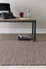 Living room scene with a Lingo Brown Trellis rug under a table with a typewriter, books, and coffee mug. Styleshot