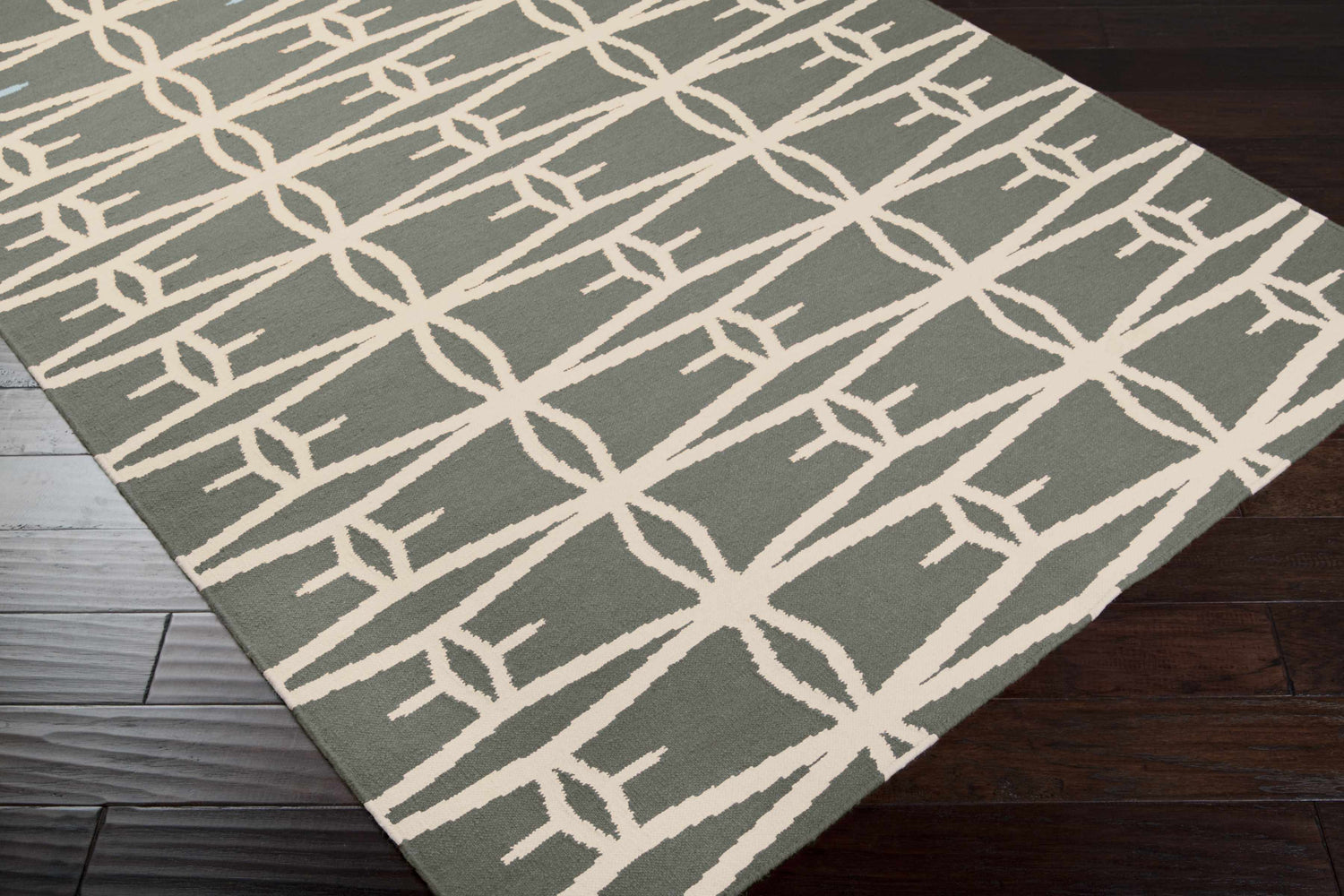 Close-up of the charcoal Lipan Area Rug. Contemporary geometric design in charcoal and peach on dark wood floor. Corner