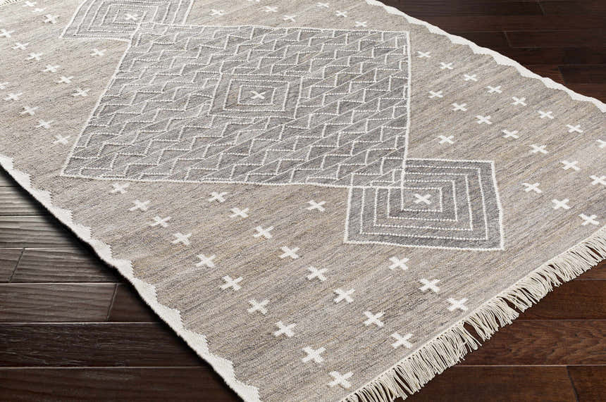 Close-up of the Lodwar Area Rug. Hand-woven rug in charcoal, cream, and gray with geometric and cross patterns. Corner
