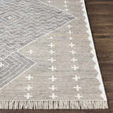 Close-up of Lodwar Area Rug showing charcoal, cream, and gray geometric pattern and fringe detail on dark wood floor. Front