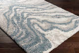 Close-up of the Lottery Area Rug; a blue and cream shag rug with a contemporary, abstract pattern. Corner