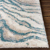 Close-up of the Lottery Area Rug. Shag rug with blue, cream, light beige, and light gray wavy pattern on dark wood floor. Front