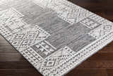 Close-up of the Luddenham textured outdoor rug. Gray rug with a geometric white pattern on dark wood floors. Corner