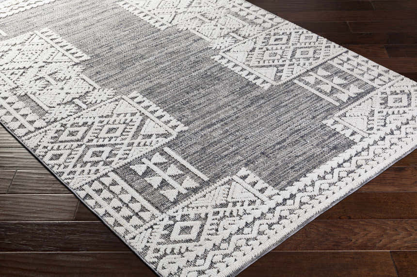 Close-up of the Luddenham textured outdoor rug. Gray rug with a geometric white pattern on dark wood floors. Corner