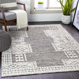 Living room scene with gray chair and the Luddenham Textured Outdoor Rug in black, gray, and white. Roomscene-Rectangle