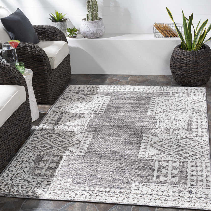 Outdoor patio scene with gray wicker chairs and a Luddenham Textured Outdoor Rug in black, gray, and white. Roomscene-Rectangle