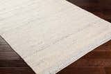 Close-up of the hand woven Lumatil Area Rug. Jute and wool rug in cream, light beige, and light gray on dark wood floors. Corner