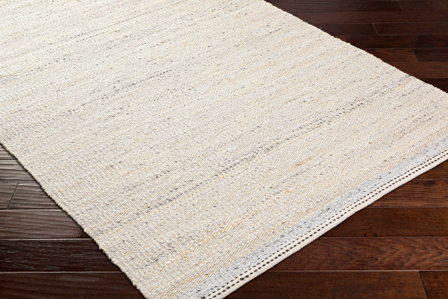 Close-up of the hand woven Lumatil Area Rug. Jute and wool rug in cream, light beige, and light gray on dark wood floors. Corner