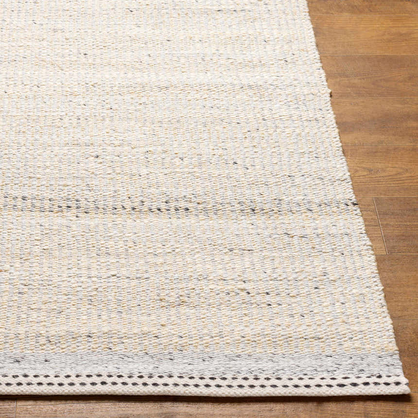 Close-up of the hand-woven Lumatil Area Rug. Jute and wool rug in cream, light gray, and beige with a black border. Front