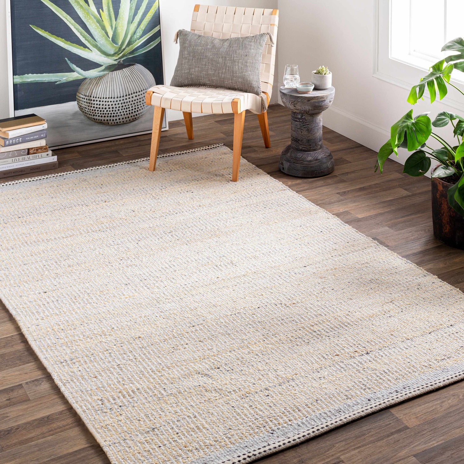 Living room scene with a cream and light beige Lumatil Area Rug, woven chair, art, and plants. Roomscene-Rectangle