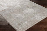 Close-up of the Lumbia Distressed Embossed Area Rug. Neutral beige tones with a subtle, textured pattern on dark wood flooring. Corner