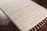Close-up of the cream and gray Luncarty Area Rug with geometric pattern and tassels on dark wood floors. Corner