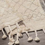 Close-up of the hand woven Luncarty Area Rug. Cream cotton rug with gray geometric pattern and braided tassels. Fold
