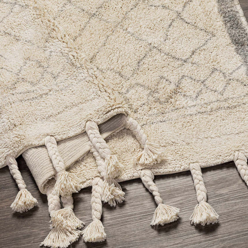 Close-up of the hand woven Luncarty Area Rug. Cream cotton rug with gray geometric pattern and braided tassels. Fold