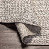 Close-up of the Lusacan Area Carpet showing its charcoal and off-white geometric pattern and hand-knotted texture. Fold