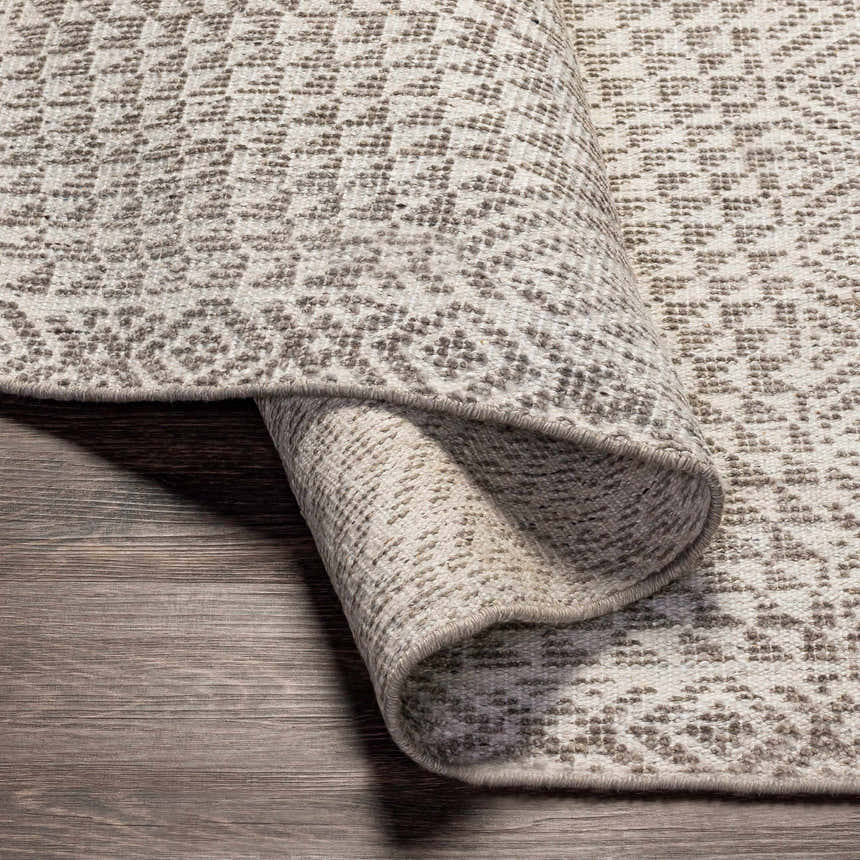 Close-up of the Lusacan Area Carpet showing its charcoal and off-white geometric pattern and hand-knotted texture. Fold