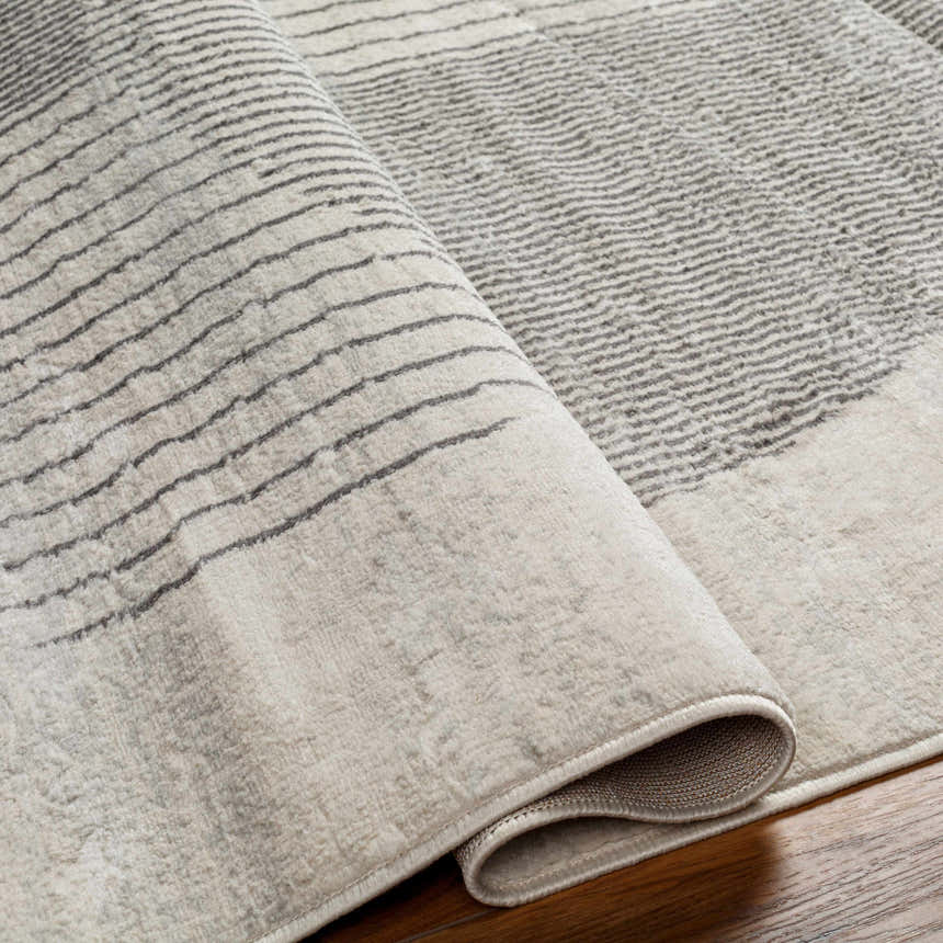 Close up of the Elvi Area Rug in natural gray, with a subtle geometric striped pattern and soft, textured pile. Fold