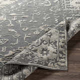 Close-up of the hand-loomed Macgregor Area Rug. Charcoal gray rug with light gray, bohemian-style pattern and textured pile. Fold