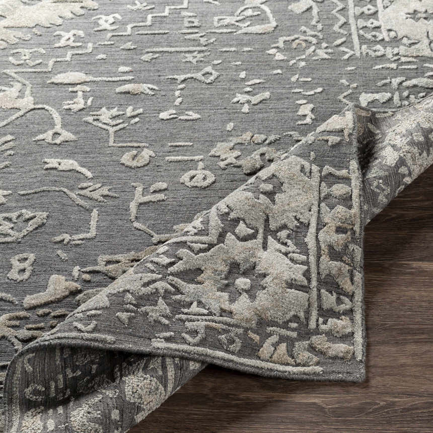 Close-up of the hand-loomed Macgregor Area Rug. Charcoal gray rug with light gray, bohemian-style pattern and textured pile. Fold