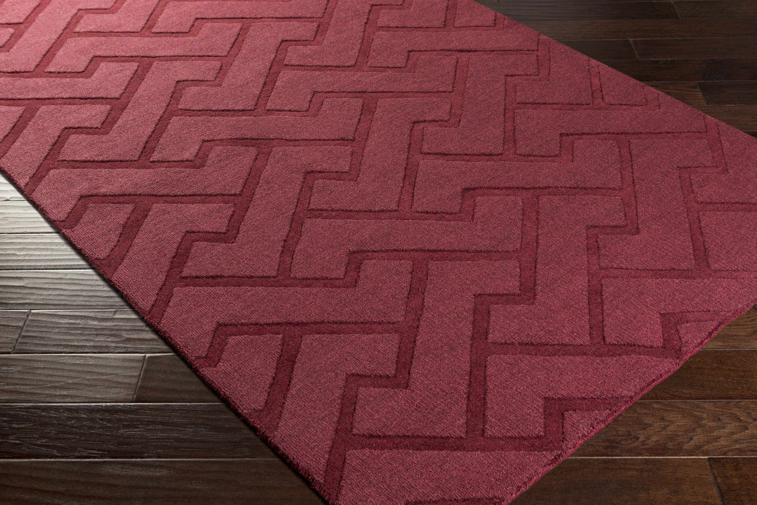 Close-up of the plum Magness Area Rug showing its geometric pattern and hand-loomed texture on a dark wood floor. Corner