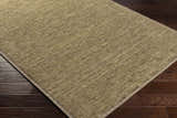 Close-up of the hand-loomed Magpet Area Rug in olive. 100% wool rug with subtle texture on dark wood floors. Corner