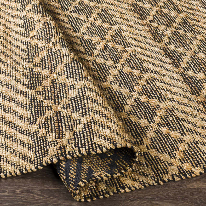 Close-up of the hand-woven Malidong Jute Carpet. Black and tan geometric pattern with a textured, bohemian style. Fold
