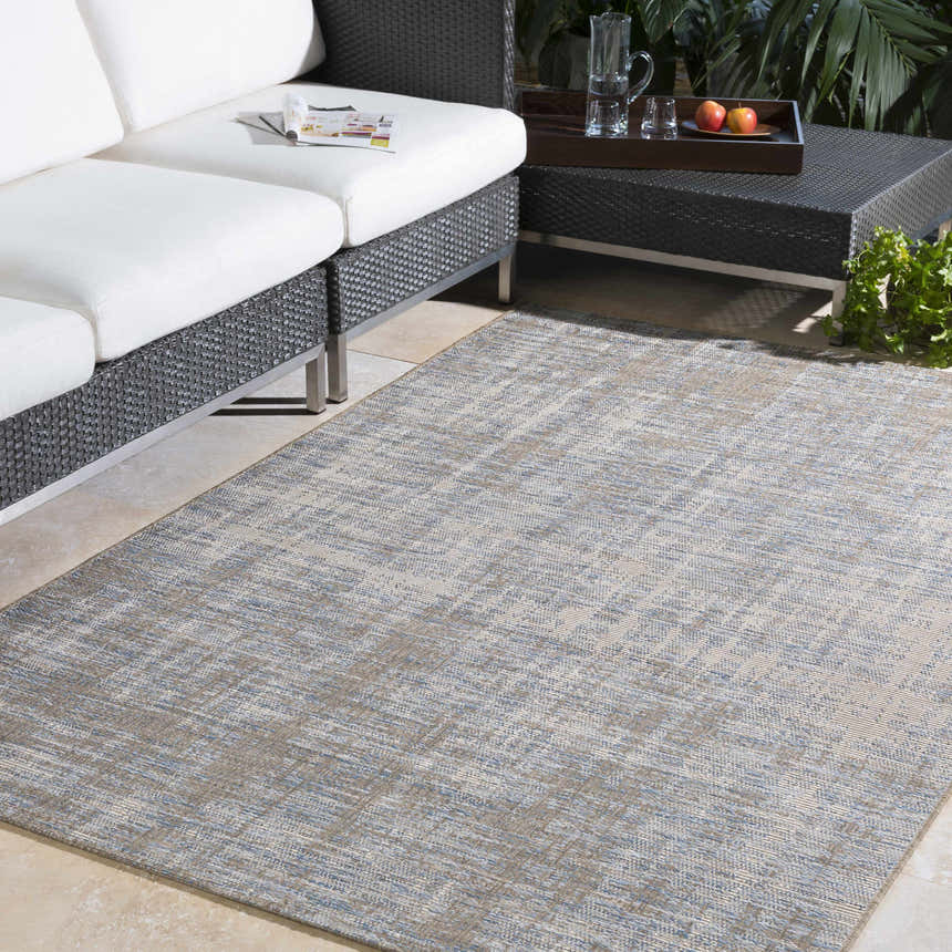 Outdoor patio scene with a blue and cream Manzanita Area Rug, wicker furniture, and neutral tile flooring. Roomscene-Rectangle