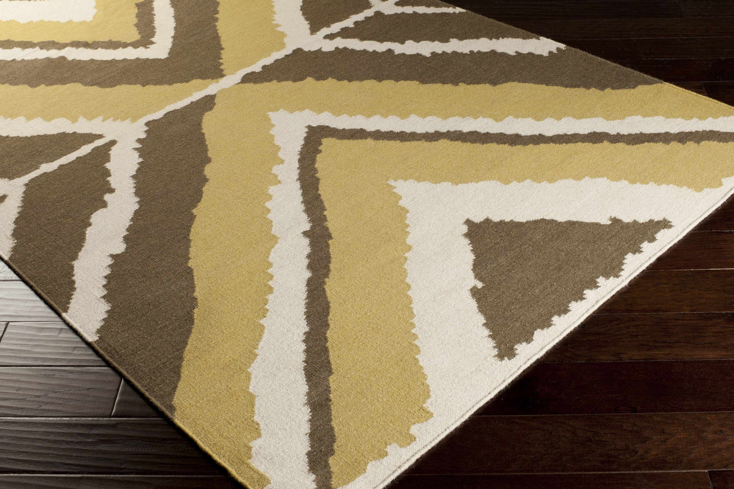 Close up of the Marysville Carpet, a hand woven wool rug in light beige, olive, and brown on dark wood floors. Corner