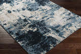 Close up of the Masiga Washable Area Rug. Contemporary style with blue, black, and beige abstract pattern on a dark wood floor. Corner