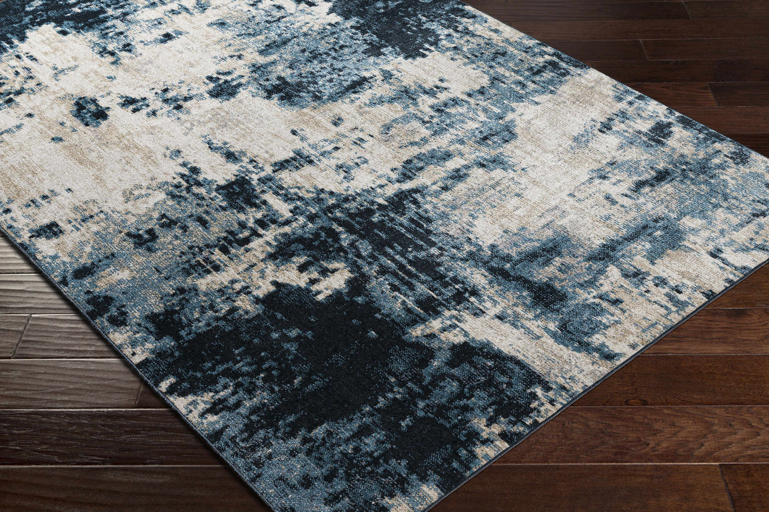 Close up of the Masiga Washable Area Rug. Contemporary style with blue, black, and beige abstract pattern on a dark wood floor. Corner