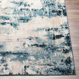 Close up of Masiga Washable Area Rug showing abstract design in shades of blue, beige, and black on wood floor. Front