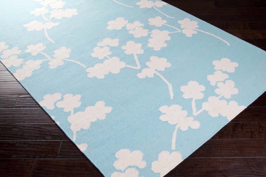 Close-up of Matador Area Carpet in aqua and light beige. Features a floral branch design on dark wood floors. Corner