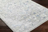 Close-up of the Mateo Area Rug. Light gray rug with pale slate and metallic silver traditional design. Corner
