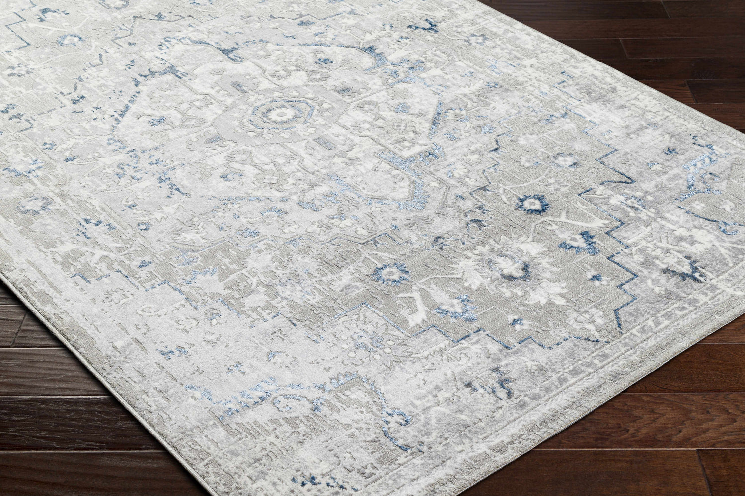 Close-up of the Mateo Area Rug. Light gray rug with pale slate and metallic silver traditional design. Corner