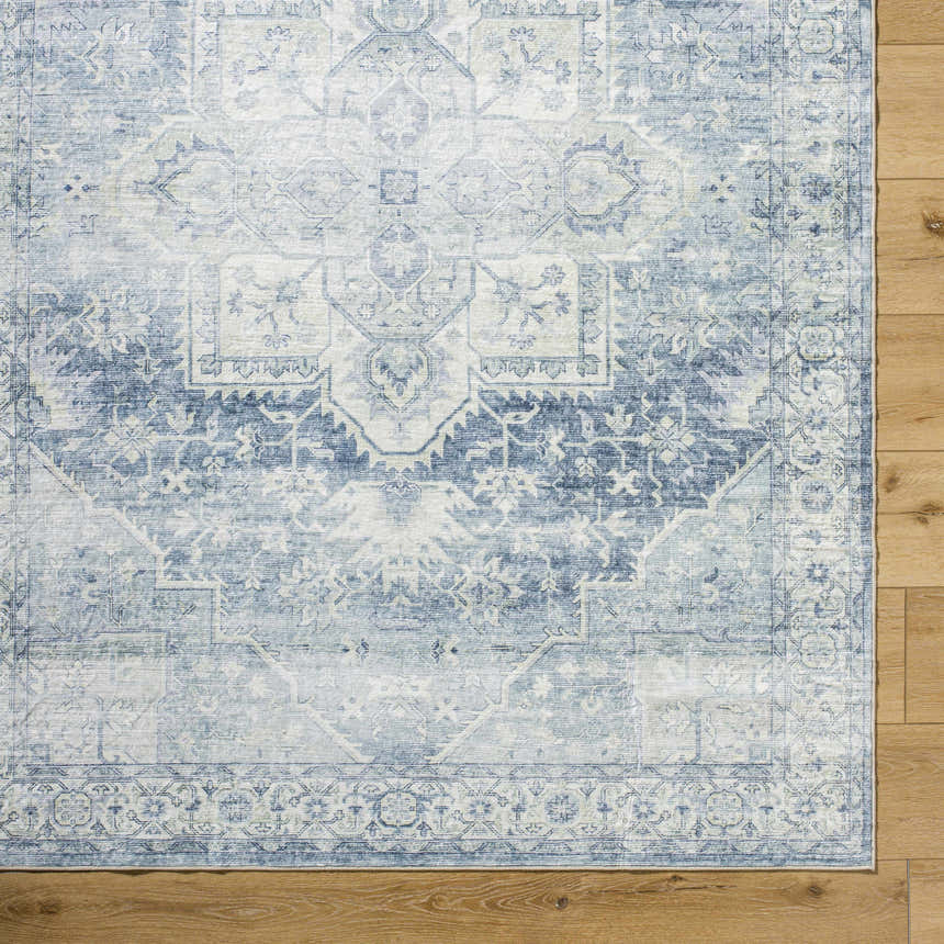 Close-up of the Mauro Navy Medallion Washable Area Rug, showing its traditional blue and gray pattern on a wood floor. Corner