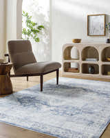 Living room scene with a Mauro Navy Medallion Washable Area Rug, gray chair, and decorative shelving unit. Roomscene-Rectangle