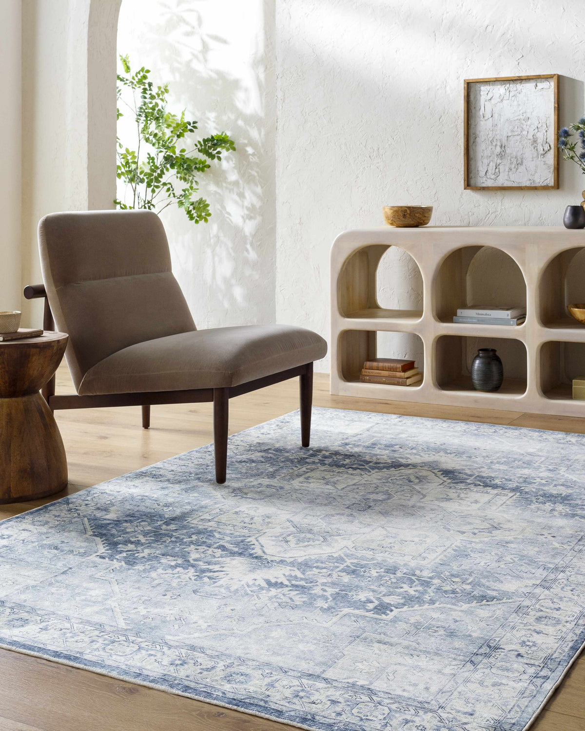 Living room scene with a Mauro Navy Medallion Washable Area Rug, gray chair, and decorative shelving unit. Roomscene-Rectangle